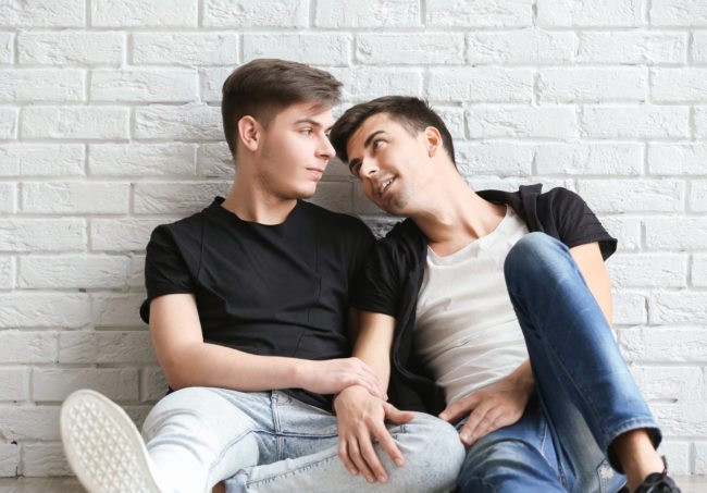  Couple gay heureux assis sur un fond de mur de briques blanches 