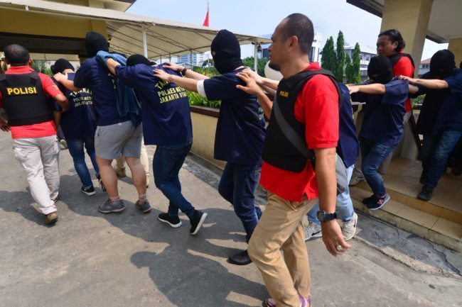 Indonesian police guard men arrested in a recent raid during a press conference at a police station in Jakarta on May 22, 2017. Indonesian police have detained 141 men who were allegedly holding a gay party at a sauna, an official said on May 22, the latest sign of a backlash against homosexuals in the Muslim-majority country. / AFP PHOTO / FERNANDO (Photo credit should read FERNANDO/AFP/Getty Images)