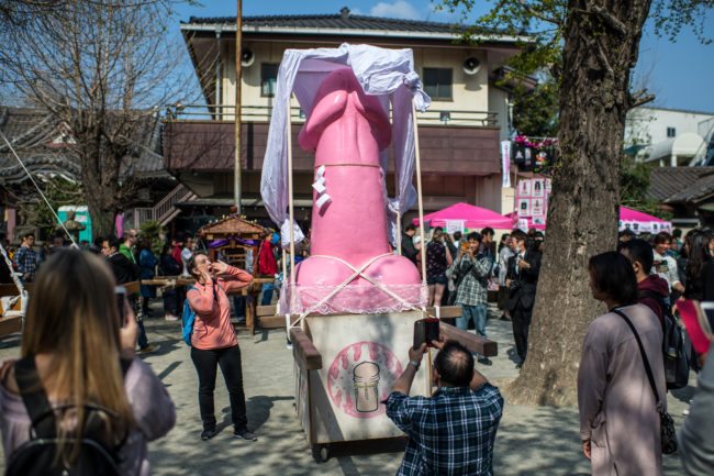 KAWASAKI, JAPAN - APRIL 01: (EDITORS NOTE: Image contains suggestive content.) A tourist poses for a photograph next to a large pink phallic-shaped 'Mikoshi' before it is paraded through the streets during Kanamara Matsuri (Festival of the Steel Phallus) on April 1, 2018 in Kawasaki, Japan. The Kanamara Festival is held annually on the first Sunday of April. The penis is the central theme of the festival, focused at the local penis-venerating shrine which was once frequented by prostitutes who came to pray for business prosperity and protection against sexually transmitted diseases. Today the festival has become a popular tourist attraction and is used to raise money for HIV awareness and research. (Photo by Carl Court/Getty Images)