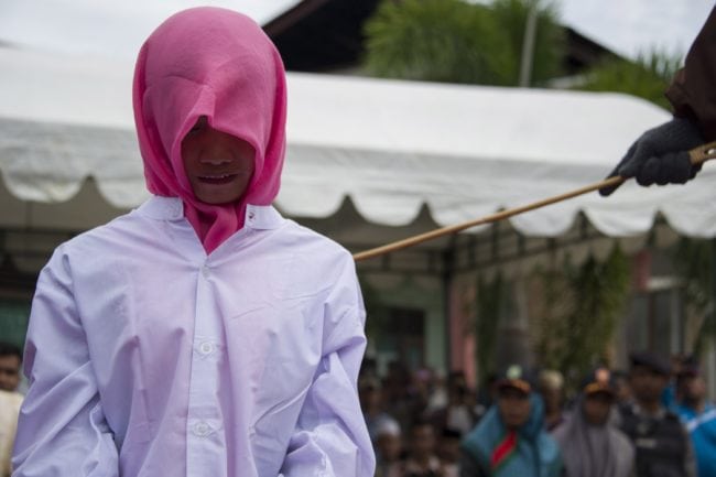 An Acehnese woman convicted for "immoral acts" reacts after being lashed by a hooded local government officer during a public caning at a square in Banda Aceh, Aceh province, on June 12, 2015. AFP PHOTO / Chaideer MAHYUDDIN        (Photo credit should read CHAIDEER MAHYUDDIN/AFP/Getty Images)