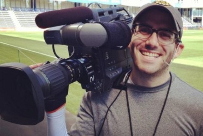 Scott Winer poses with a camera in a sports ground
