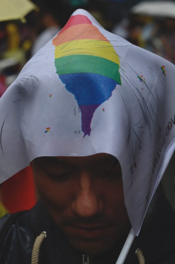 A gay rights supporter hide under a flag while waiting for the results under the rain outside Parliament while law makers discusses the same sex marriage bill in Taipei on May 17, 2019.