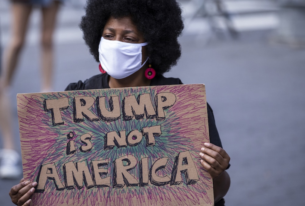 A protester wearing a face mask holds a homemade sign that says, "Trump is Not America"