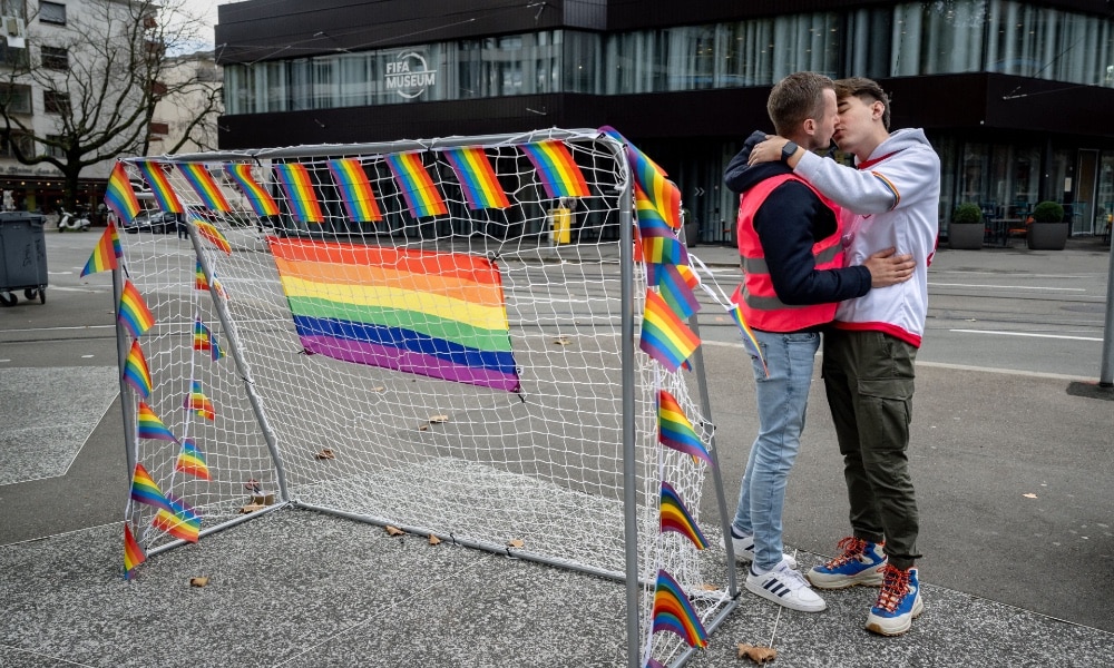 Two men kiss in Zurich by goalpost and rainbow flags